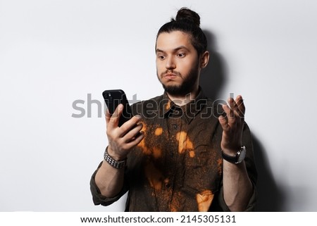 Surprised young man, with hair bun, looking in smartphone on white background.