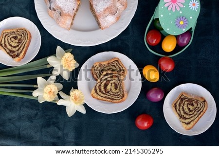 Bread texture of sliced potica, sweet bread roll stuffed with poppy seeds and raisins.  Small plates with Easter cake slices with remaining Easter bread cake, Easter eggs and flowers in background.