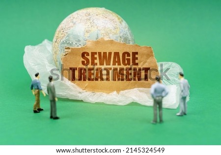 Ecological concept. On a green background on a plastic bag is a globe and a sign with the inscription - Sewage treatment. Near out of focus figures of people