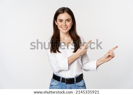 Portrait of smiling confident woman, business girl showing advertisement, pointing fingers right at logo, banner or announcement, standing over white background