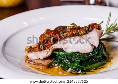 White fish in creamy sauce with spinach on a white plate