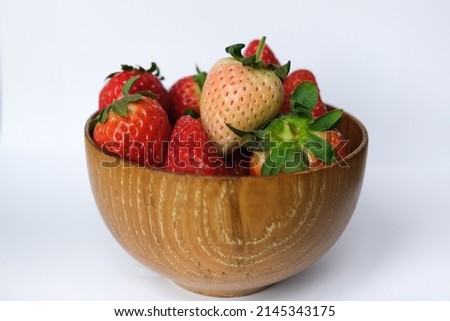 Red strawberries and one white and pink strawberry (pineberry) in a wooden bowl on white background