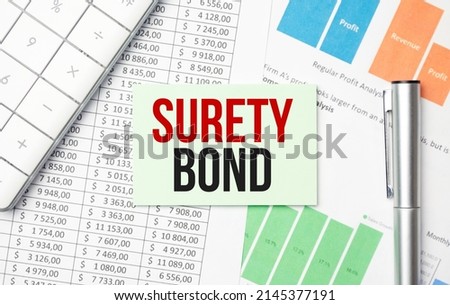 On the desktop there are reports, notepads, a calculator, a cash and a yellow sticker with the text SURETY BOND. Business concept Royalty-Free Stock Photo #2145377191