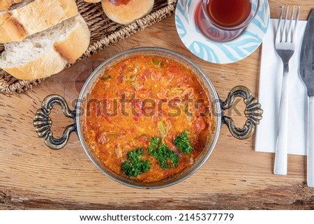 Ingredients in Menemen frying pan and on the table. Famous Turkish menemen dinner on table, made by eggs, pepper and tomatoes. Royalty-Free Stock Photo #2145377779