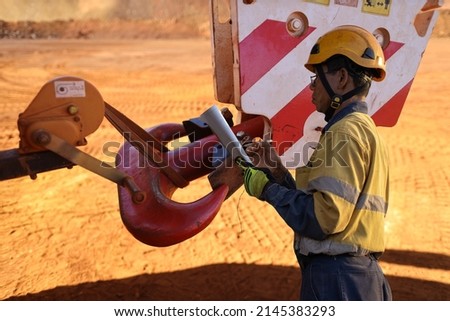 Asian rigger high risk worker wearing helmet glove inspector conducting inspecting checking crane lifting hook prior lifting construction building site, Australia 

