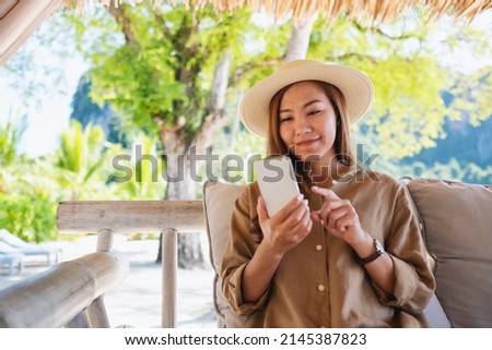 Portrait image of a beautiful young asian woman holding and using mobile phone while sitting in the outdoors