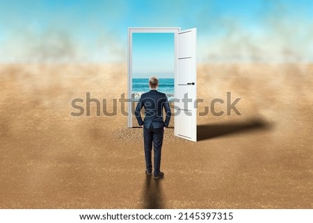 A man in front of an open door in the desert. New beginning, new life, vacation, travel, vacation. Door in the desert, access to the beach, blue sea. Hope, dream, goal Royalty-Free Stock Photo #2145397315