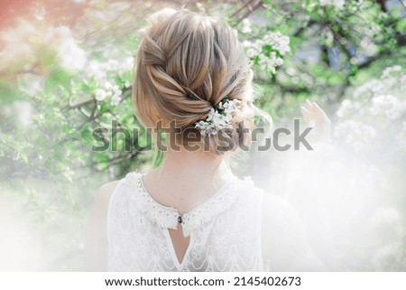 Art work hairstyles with weaving for a blonde bride in a blooming spring garden with green leaves Royalty-Free Stock Photo #2145402673