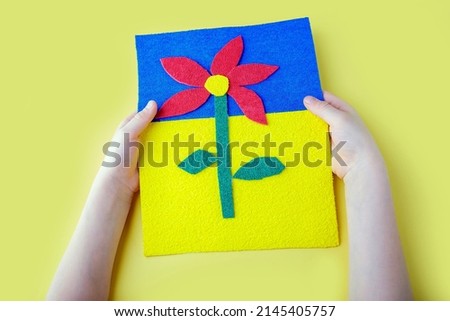 DIY and kid's creativity. Child hands hold crafts picture with flower cut out of fabric. Gift for mother day