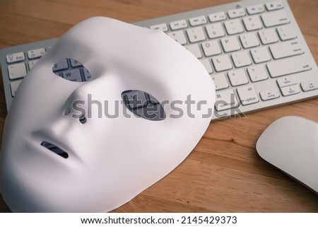White scary half face mask, keyboard and mouse on wooden table background in dark tone. Hacker, cybercrime, romance scam and online security concept. Royalty-Free Stock Photo #2145429373