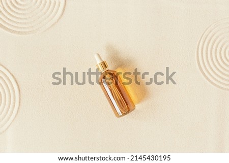 Serum or liquid collagen dropper bottle on sand background. Anti age cosmetics products. Skin care beauty products, summer concept. Japanese zen garden with rounds on sand. Above view, beige color