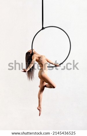 Full body side view of flexible female gymnast doing walking pose on aerial hoop against white background in light studio Royalty-Free Stock Photo #2145436525