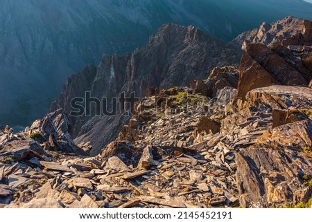 Awesome mountain view from cliff at very high altitude. Scenic landscape with beautiful sharp rocks near precipice and couloirs in sunlight. Beautiful mountain scenery on abyss edge with sharp stones. Royalty-Free Stock Photo #2145452191