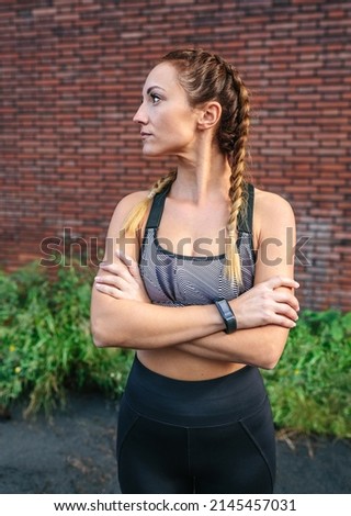 Sporty woman with crossed arms posing in front of a brick wall