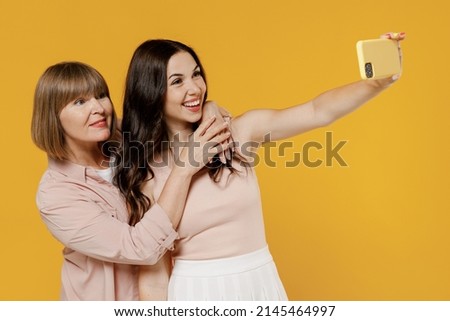 Two side view young happy smiling daughter mother together couple women in casual clothes doing selfie shot on mobile cell phone post photo on social network isolated on plain yellow background studio