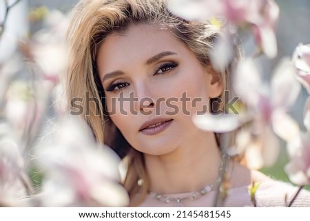 Portrait of a beautiful happy middle aged woman enjoying the smell in a blooming spring garden. Beautiful magnolia bushes, large flowers.