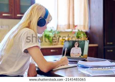 Teenage female student in headphones sitting at home using laptop talking to teacher