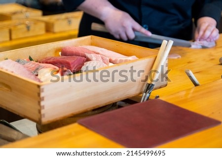 Close-up selective focus sashimi box with blurred sushi chef using knife cutting sashimi on the background.
