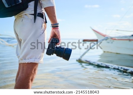 Photography and travel. Close up of young man holding camera enjoying beautiful sea view on fishing beach.