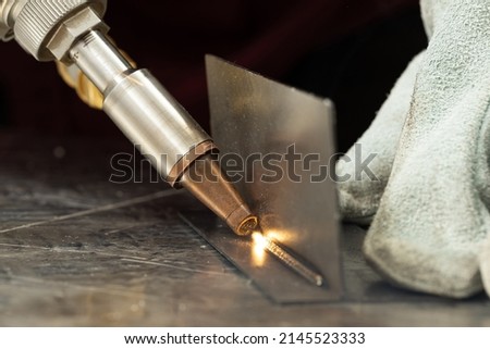 A man in gloves at the enterprise welds metal products by laser welding on a metal workbench. sparks fly Royalty-Free Stock Photo #2145523333
