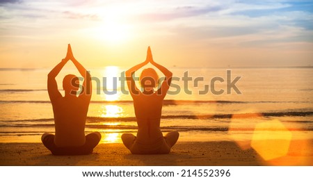 Yoga silhouette of a young couple on the beach at sunset.