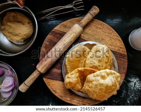 Stock photo of delicious hot deep fried puri or bhatura made up by wheat flour or all purpose flour kept in steel plate for serving. wooden rolling board ,pin and other utensils anon background.