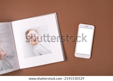 Baby's photo book and mobile phone mock up on brown background . Children's emotional portrait.Cute toddler boy