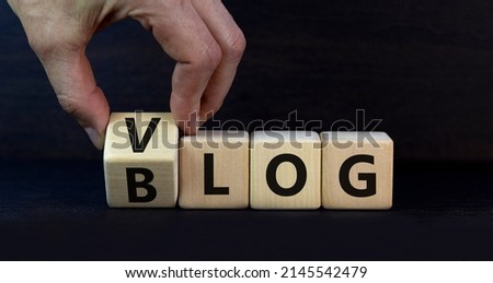 Blog or Vlog symbol. Businessman turns wooden cubes and changes the word Blog to Vlog. Beautiful grey table grey background. Business and information blog or vlog concept. Copy space.