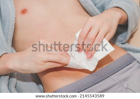 The hands of a caucasian young man wipe the small intestine with a sticky circle on the stomach with a sterile and dry napkin,  top view. The concept of a step-by-step replacement of a bedbug-colostom