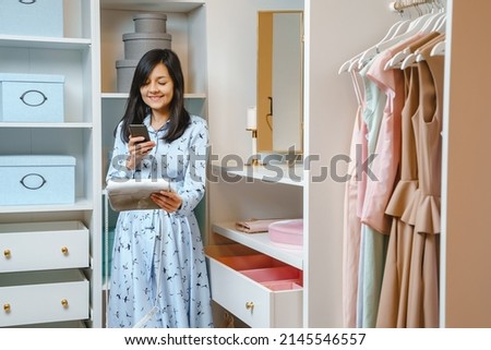 Attractive young woman making photo of handbag on smartphone in dressing room. Fashion and style concept.