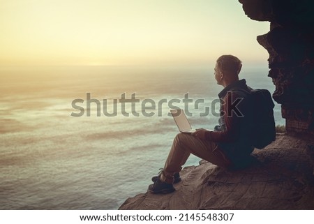 Connecting to the world. Full length shot of a young man using his laptop while sitting on a cliff in the mountains. Royalty-Free Stock Photo #2145548307