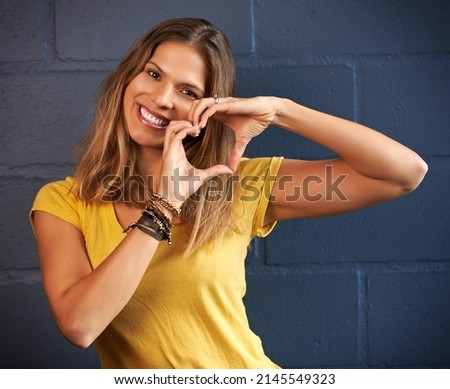 I heart you this much. Portrait of a young woman making a heart gesture with her hands against a brick wall background.