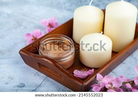 Glass cosmetic  jar of cream, decorative flowers and candles on a tray on a marble background. Natural organic cosmetics. Spa products for health and beauty. Serum, face oil.