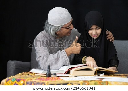 muslim father teaching his daughter about practicing reading textbook and thumbs up pose on black background