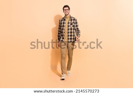 Full length body size view of attractive cheerful guy wearing checked shirt walking isolated over beige pastel color background Royalty-Free Stock Photo #2145570273