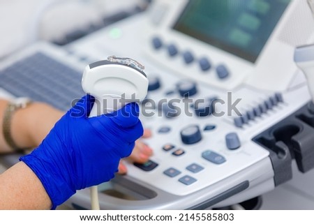 Close up of ultrasonography equipment, doctor hand in rubber gloves, holding ultrasound probe with coupling gel prepare for scanning. Special technology button for sonogram. Royalty-Free Stock Photo #2145585803