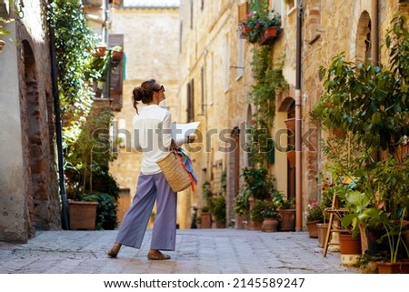 Travel in Italy. Seen from behind stylish woman with map and straw bag enjoying promenade in Tuscany, Italy. Royalty-Free Stock Photo #2145589247