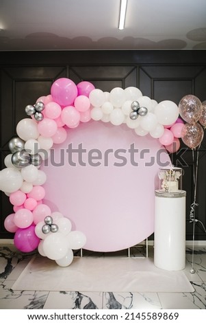 Arch decorated with pink, white and silver balloons. Baby shower party. Trendy Cake with a figure angel for a girl. Copy space. Celebration baptism concept. Birthday Cake on a background photo wall.