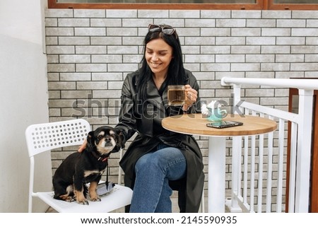 beautiful girl model eats in a cafe on the street with a black dog. hugs, loves. light background. High quality photo