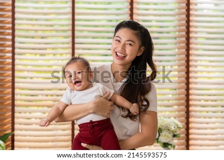 Happy asian mom playing and spending time with her newborn baby and looking at camera together at home.Adorable baby boy smile laughing with mother in warmth place relax and comfortable.good moment Royalty-Free Stock Photo #2145593575
