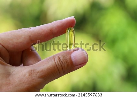 Soft capsule of fish oil hold by two fingers isolated on green bokeh background