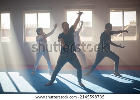 Coach showing Tai Chi exercise to students. Male trainer standing in front of senior people and moving arms at grou class. Martial art concept Royalty-Free Stock Photo #2145598735