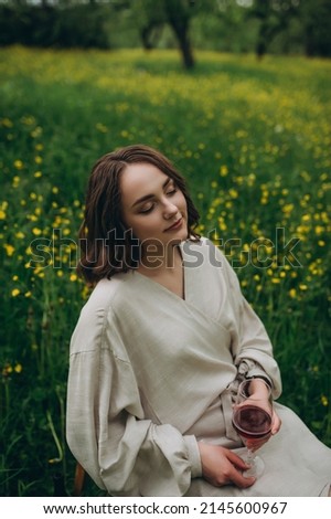 Beautiful woman in a white dress. The girl is sitting in the botanical garden and tasting red wine.