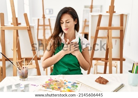 Beautiful caucasian woman at art studio smiling with hands on chest with closed eyes and grateful gesture on face. health concept. 
