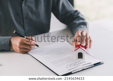 Close up wooden toy house with man signs a purchase contract or mortgage for a home, Real estate concept.