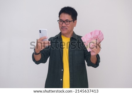 A man holds some money and a smartphone; smiling.