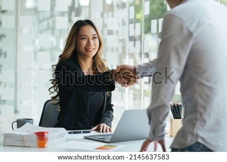 Smiling asian manager sitting at her desk in an office shaking hands with a job applicant after an interview