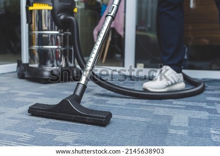 A man cleans the carpet flooring of an office with an upright vacuum cleaner with an attached upholstery nozzle. Royalty-Free Stock Photo #2145638903