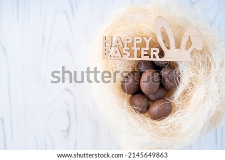 a nest with chocolate eggs and rabbit ears with the inscription Happy Easter. white background