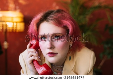 Young fashion stylish woman standing at chair vintage studio, posing with retro phone, bright make up and colored hair